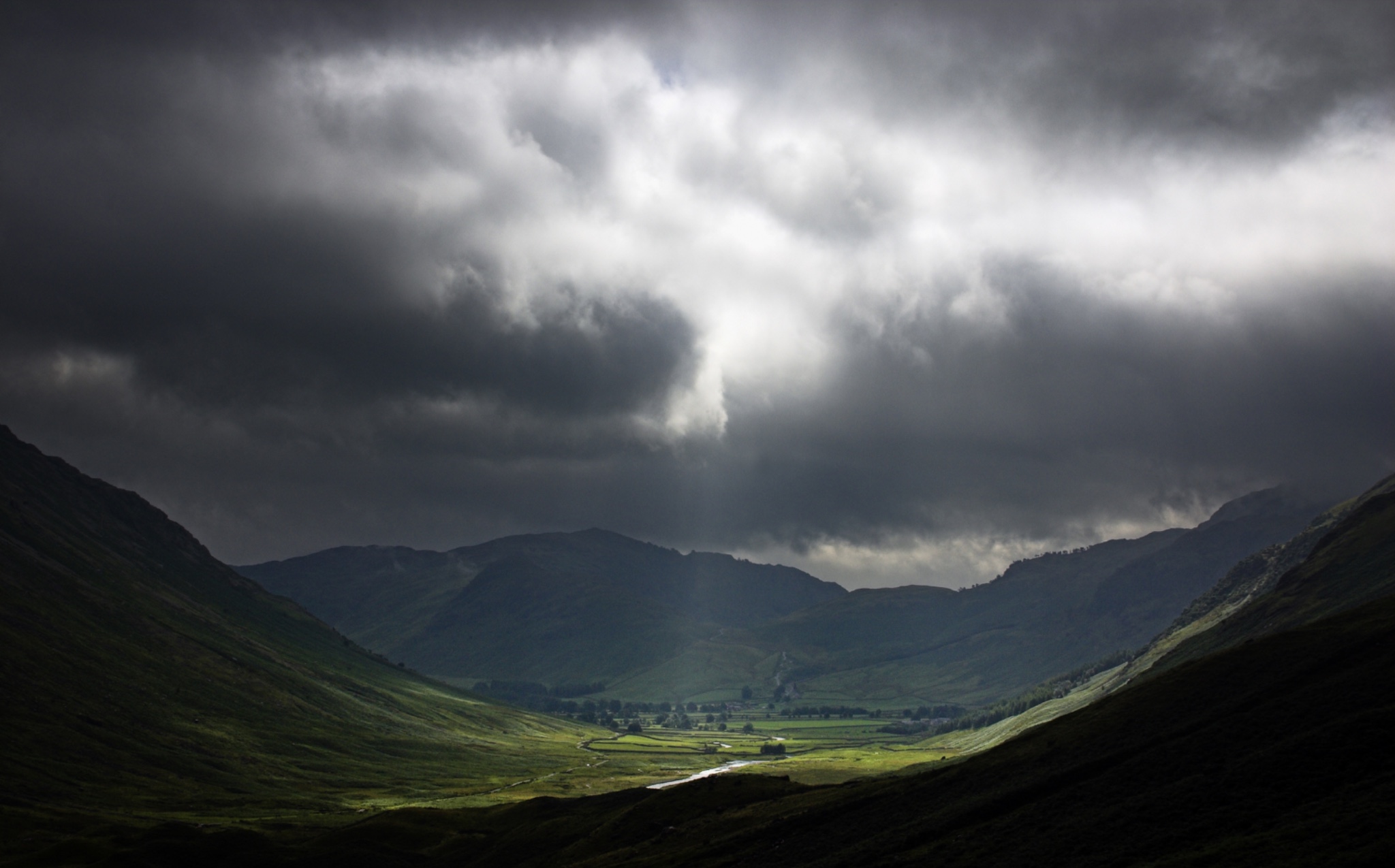 ENGLANDCumbriaLakeDistrictNationalPark.AbreakinthestormcloudsilluminatestheMickledenandsurroundingLangdalemountainsontheCumbriaWay